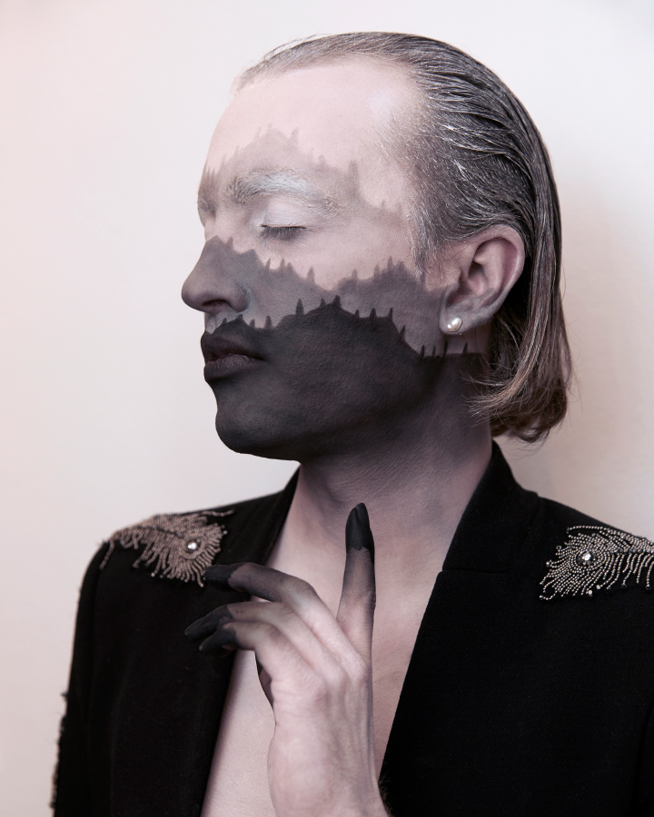 Jesse Clark posing with black and white facepaint that resembles a mountain range against a white background.